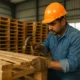 Worker repairing a wooden pallet inside a warehouse as part of the recycling wooden pallets process.